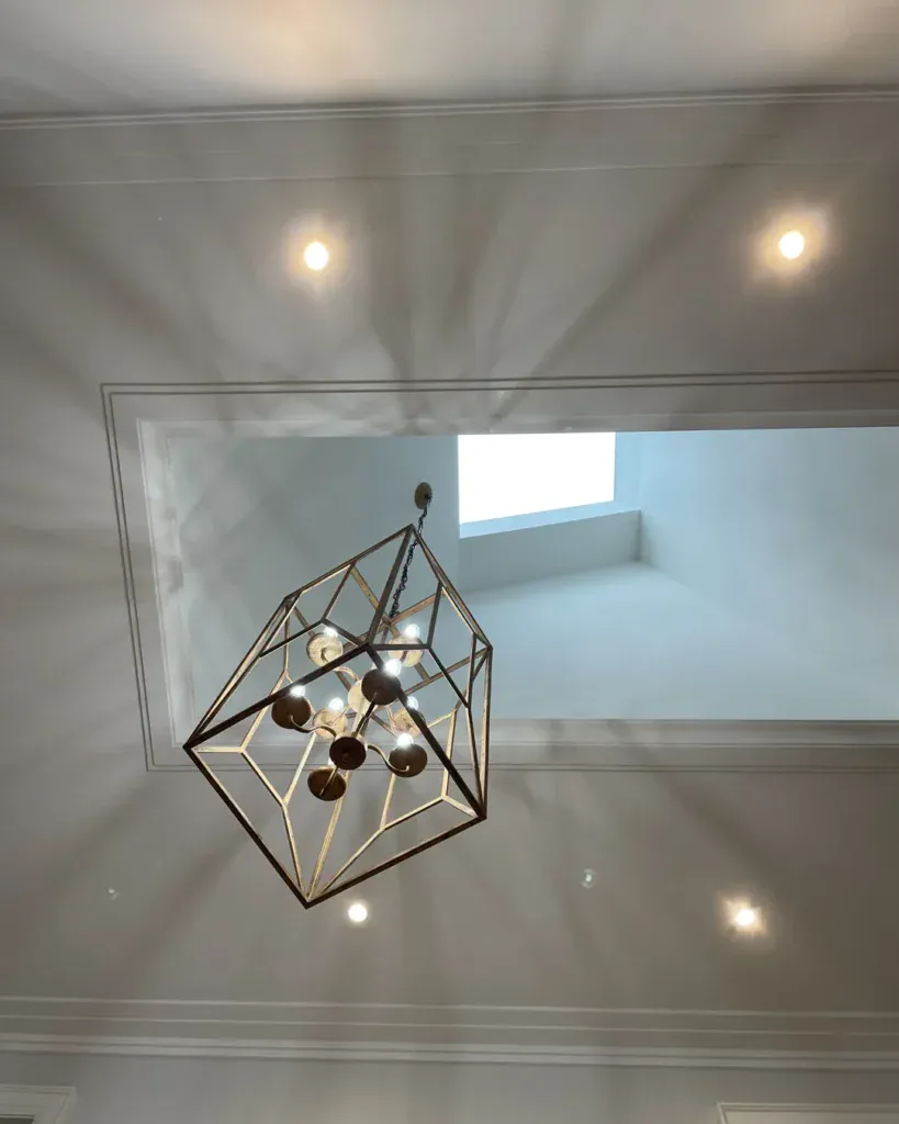 Pot lights and a geometric pendant light installed under a skylight by Padi Electric